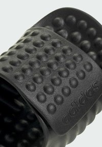 Sort svinesandal med en tekstureret, bumpet strop og præget logo. Lavet af syntetisk materiale med en polstret design.