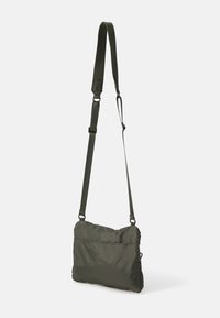 Borsa a tracolla verde oliva realizzata in tessuto leggero, dotata di una tracolla removibile, texture morbida e una tasca posteriore con zip.