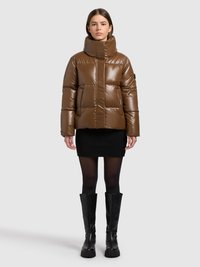 Brun vadderad jacka med hög krage och glänsande yta, med en ficka med dragkedja och kvadratisk quiltad design. Matchad med en svart minikjol och knähöga stövlar.