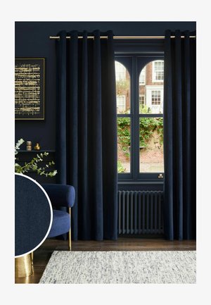 Dunkelblaue Samtvorhänge, die ein hohes bogenförmiges Fenster in einem Zimmer mit einem blauen Stuhl und einem hell gemusterten Teppich teilweise bedecken.