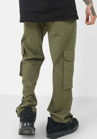 Olijfgroene cargo pants met meerdere zakken, gemaakt van duurzaam materiaal. Gestyled met een losse pasvorm, gecombineerd met zwarte sportschoenen.
