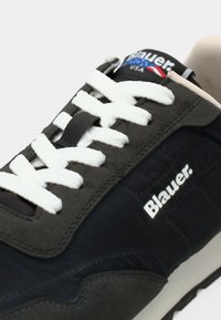 Baskets gris foncé avec des lacets blancs, présentant une tige texturée, une languette brandée et une semelle contrastée noire et blanche.