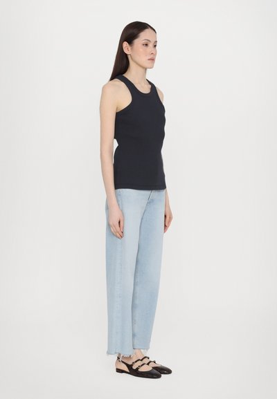 Débardeur marine en tissu côtelé, associé à un jean bleu clair taille haute et des chaussures à bride arrière noires avec des accents beiges.