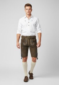Traditionelt dirndl-outfit bestående af en hvid langærmet skjorte med plisséer, brune lædershorts med broderi og knælange cremefarvede sokker.