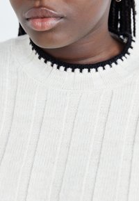 Light gray ribbed sweater with a black scalloped collar, showcasing a textured knit pattern. Close-up of neckline area.