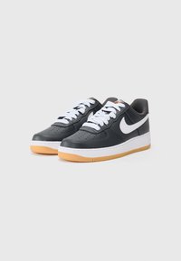 Čierne kožené tenisky s bielymi šnúrkami a logom Nike Swoosh. Majú bielu medzipodrážku a podrážku z gumy, navrhnuté s perforáciami.