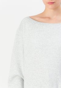 Felpa oversized grigia chiara con una vestibilità ampia, scollo largo e polsini a coste. Tessuto morbido e strutturato.