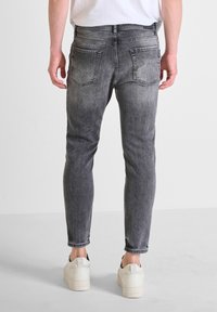 Bleka grå denimjeans med slim fit, fem fickor och sömdekor, bärs med vita sneakers. Bakvyn visar upp det strukturerade materialet.