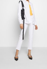 Chaqueta y pantalones de denim blancos, blusa naranja, bolso negro con correa, bailarinas negras de punta decoradas. Diseño simple y moderno.