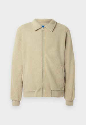 Beige fleece jacket with a zip front, stand collar, two side pockets, ribbed cuffs, and hem. The texture appears soft and cozy.