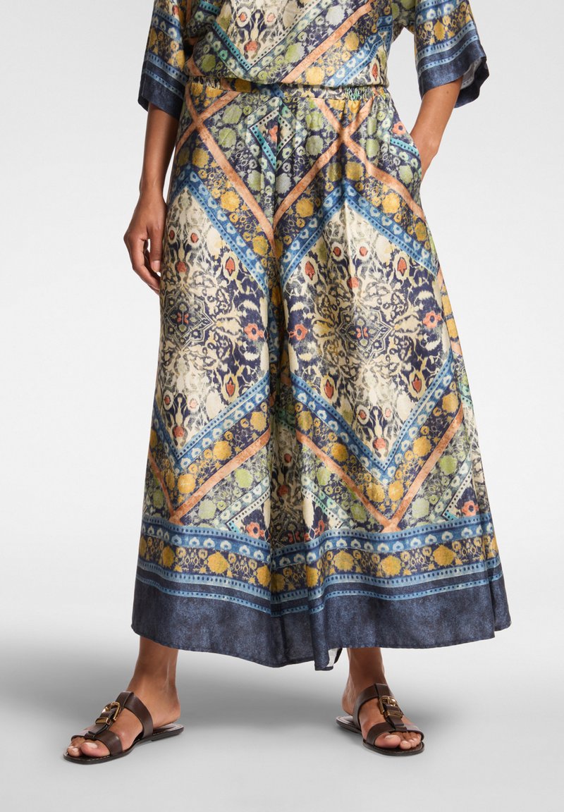 Maxi sukně z lehkého materiálu s barevným geometrickým vzorem v modré, zelené a oranžové barvě; elastický pas a boční kapsy.
