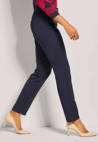 Marineblauwe pantalon met een rechte pijp, gladde stof en zijsplitten, gecombineerd met beige hoge hakken.