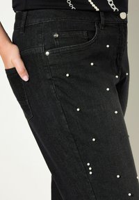 Černé džíny z denimu s perlovými ozdobami, pěticípkovým designem a kovovými detaily. Hladká textura s přiléhavým střihem.