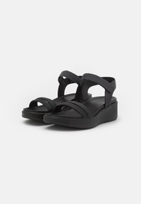 Sandalias negras con suela de plataforma, que presentan tiras entrelazadas y una textura suave. Diseño minimalista sin detalles visibles de herrajes.