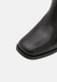 Black leather ankle boot with a smooth texture, rounded toe, and a low-profile rubber sole. Minimalist design without visible hardware.