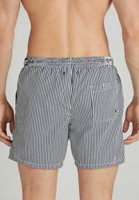 Pruhované plavky v námořnické modré a bílé barvě, s elastickým pasem, bočními kapsami a zadní kapsou s klopou a knoflíkovým zapínáním.