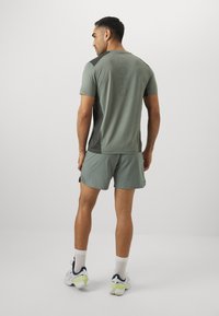 Conjunto atlético masculino en verde claro, camiseta de manga corta con acentos más oscuros y detalle de logo, combinado con pantalones cortos a juego y zapatillas deportivas.