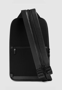 Zwarte rugzak met een strak ontwerp, gestructureerde stof, gladde leren accenten, verstelbare riemen en een voorvak met rits.