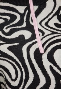Schwarz-weißer Pullover mit wirbelndem Muster, mit einem pinken Reißverschlussakzent. Hergestellt aus Strickstoff mit einer weichen Textur.