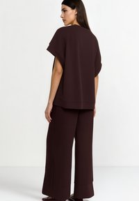 Maglietta oversize color marrone scuro con maniche corte e scollo rotondo abbinata a pantaloni a gamba larga. Tessuto liscio con dettagli di cuciture minime.