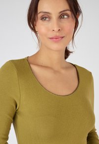 Top ajustado en verde oliva con escote redondeado, tejido texturizado y un ribete con hilo metálico a lo largo del escote.