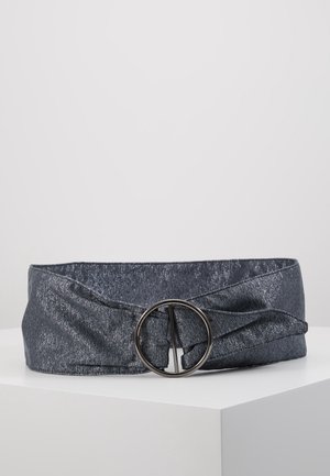 Large ceinture en tissu métallique gris foncé avec une grande boucle ronde en métal noir exposée sur une surface blanche.