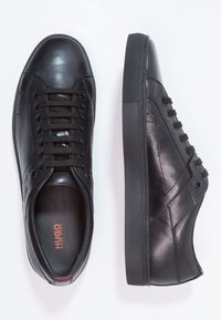 Baskets en cuir noir avec une finition lisse, un bout arrondi, une semelle en caoutchouc texturée et un design à six œillets avec lacets, ornées d'un détail logo.