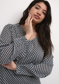 Black and white blouse with a zigzag pattern, sheer fabric, V-neckline, and long puff sleeves, featuring gathered detailing at the cuffs.