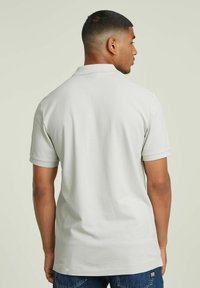 Polo de color gris claro con cuello, mangas cortas y una textura suave, que presenta un diseño limpio y sutiles detalles de costura.