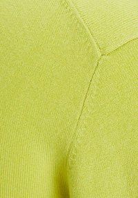 Maglione lavorato a maglia di un vivace verde lime, con una texture liscia e un primo piano della cucitura sulla spalla con una breve cucitura diagonale.