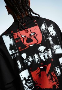 Tricou negru cu un colaj de imprimări grafice roșii și albe, inclusiv fețe și mâini, cu text îndrăzneț în mai multe stiluri.