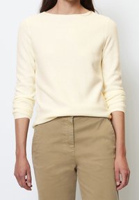 Pull côtelé jaune clair à manches longues, col rond et coupe décontractée, associé à un pantalon beige, illustrant un style casual.