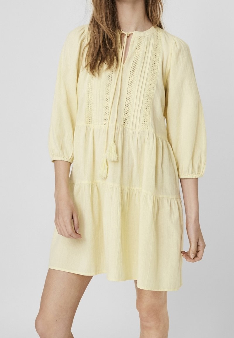 Gul, knälång klänning med trekvartslånga ärmar, texturerad tyg, knytkrage och lagerdesign med spetsdetaljer.