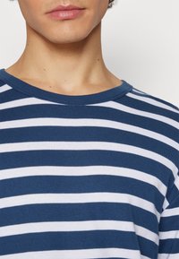 Kariertes T-Shirt aus navyblauer und weißer Baumwolle mit rundem Ausschnitt, das eine weiche Textur und ein gleichmäßiges Streifenmuster aufweist.