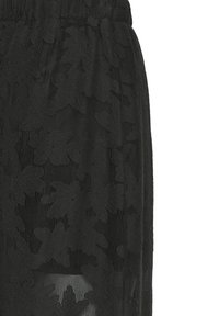 Jupe noire avec taille élastique, ornée d'une superposition en dentelle florale et de détails en tissu mesh semi-transparent.