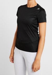 Svart atletisk t-shirt i mjuk, lätt tyg. Kort ärm, rund hals, pryds av Reebok-logotypen på vänster axel.