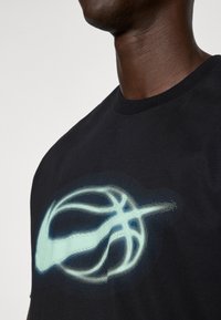 Černé bavlněné tričko s grafikou basketbalového míče ve světle modré barvě, navržené s pixelizovaným efektem pro texturu a detail.