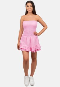 Roze strapless jurk met een gerimpeld lijfje en een gelaagde ruchesrok. Gemaakt van lichte stof, gestyled met witte sneakers.