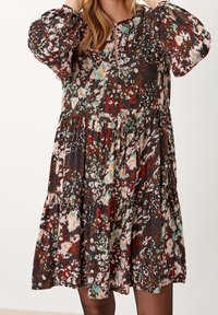 Brun blommig klänning med puffärmar, rund halsringning med en knappdetalj och en flerfärgad, lager-på-lager, svävande kjol.