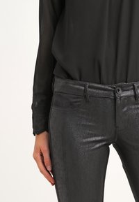 Zwarte glanzende jeans met een slim fit ontwerp, voorzien van een zachte textuur, subtiele glans en klassieke vijf-pocket styling.