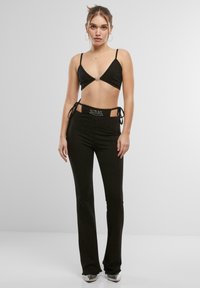 Čierny skrátený bralet s tenkými ramienkami a stredným akcentom, skombinovaný s čiernymi nohavicami s vysokým pásom, ktoré majú bočné viazanie a logo.