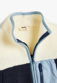 Fleecejacka med blått och marinblått färgblockdesign, texturerad, mjuk tyg. Har dragkedja och en etikett märkt "Koton Kids."
