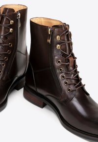 Hnědé kožené šněrovací boty na zip, se zlatými očky a nízkým dřevěným podpatkem. Hladký povrch s tónovaným prošíváním a klasický design.