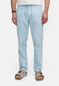 Helleblaue strukturierte Hose mit einem Kordelzugbund und seitlichen Nähten, kombiniert mit grauen Sandalen mit einer Schnalle und Korksohle.