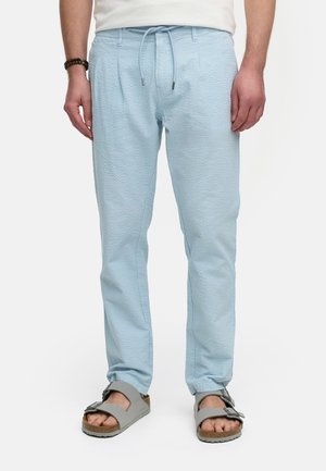Pantalones de tejido azul claro con cintura elástica y costuras laterales, combinados con sandalias grises con hebilla y suela de corcho.