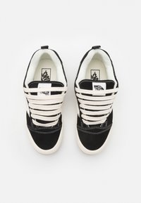Svarte semskede sneakers med hvite snørebånd, polstret krage og logo-detaljer på tungen og hælen. Har et klassisk lavt design og hvit såle.