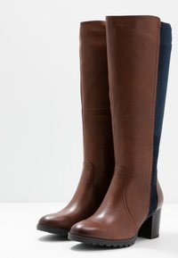 Botas de cuero marrón hasta la rodilla con panel de tela azul marino contrastante, puntera redonda, suela texturizada y tacón apilado.