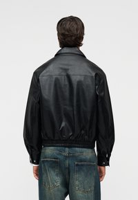 Μαύρο μπουφάν από δέρμα μπόμερ με εφαρμοστή μέση, φαρδιά γιακά και μακριά μανίκια. Η πλάτη έχει ομαλή υφή και ελάχιστες λεπτομέρειες.