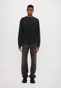 Crna pamučna košulja dugih rukava s crvenim logotipom "424", u kombinaciji s tamno sivim trapericama i crnim cipelama. Jednostavan dizajn s opuštenim krojem.