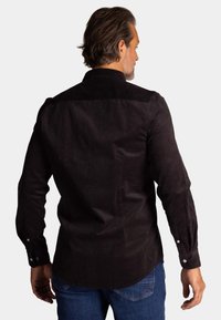 Zwarte corduroy overhemd met lange mouwen, een puntkraag en knoopmanschetten. Heeft een gladde textuur en een gebogen zoom.